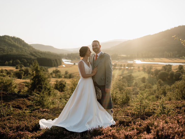 bride and groom standing in the heather with the Linn of Dee and Mar Lodge in the background 